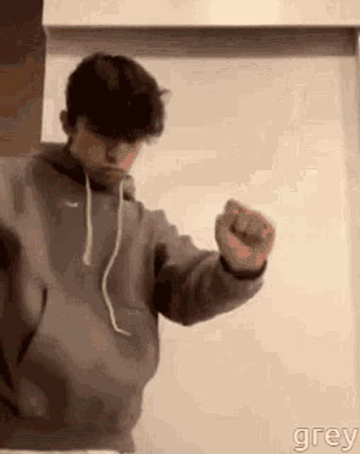 a young man in a grey hoodie is dancing in front of a white board .