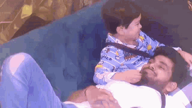 a man and a boy are laying on a blue couch .