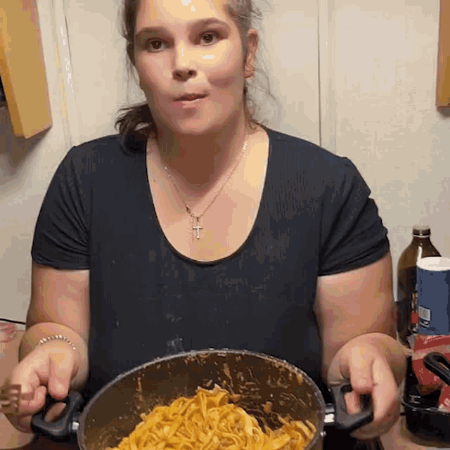 a woman in a black shirt holds a pot of noodles
