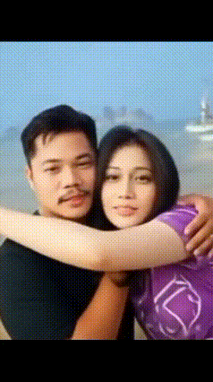 a man and a woman hugging each other with a boat in the background