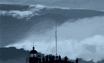 a group of people standing on top of a tower watching a large wave