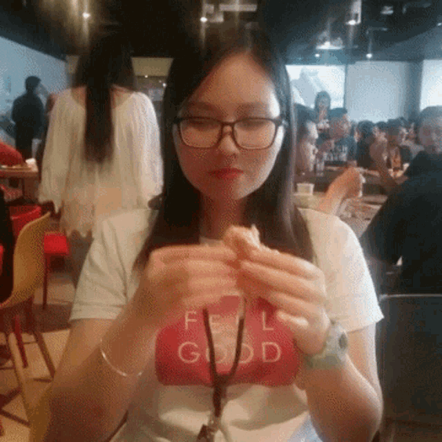 a woman wearing glasses and a t-shirt that says feel good is eating a sandwich