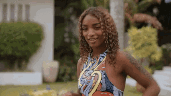 a woman with curly hair and a tattoo on her arm is wearing a colorful top