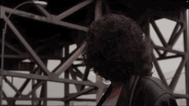 a woman with curly hair is standing in front of a bridge with a street light in the background .