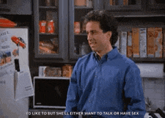 a man in a blue shirt is standing in front of a refrigerator in a kitchen talking to someone