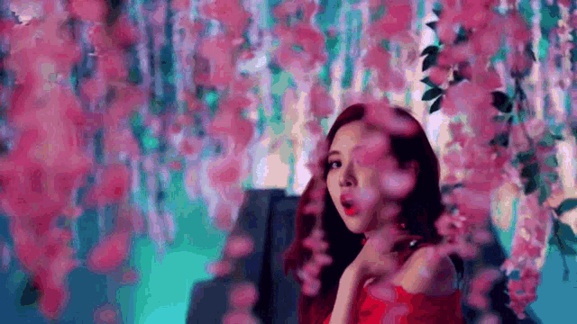 a woman in a red dress is standing in front of a row of pink flowers .