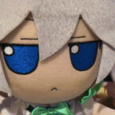 a stuffed doll with white hair and blue eyes has a green bow tie