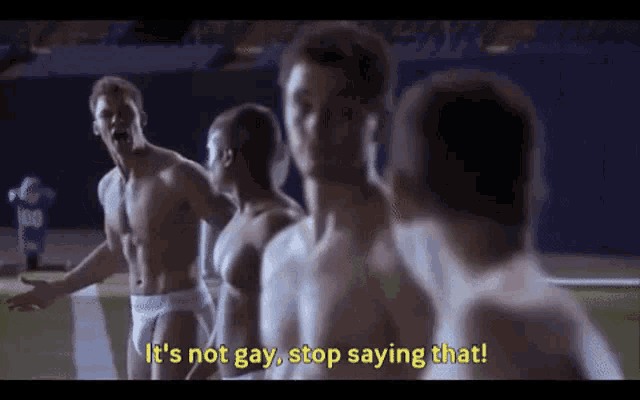 a group of shirtless men are standing on a football field and one of them is saying it 's not gay , stop saying that