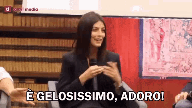 a woman is sitting in front of a microphone with the words e gelosissimo adoro written below her