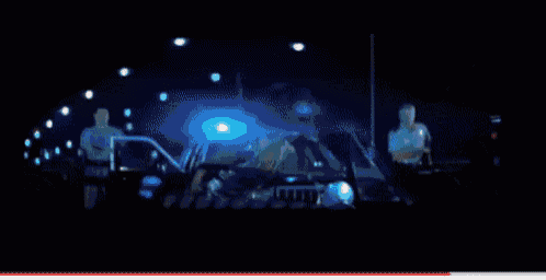 two police officers are standing in front of a police car with a blue light on it
