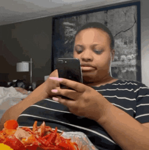 a woman is sitting on a bed looking at her phone while eating food