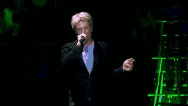 a man in a suit is singing into a microphone on a stage in front of a green background .