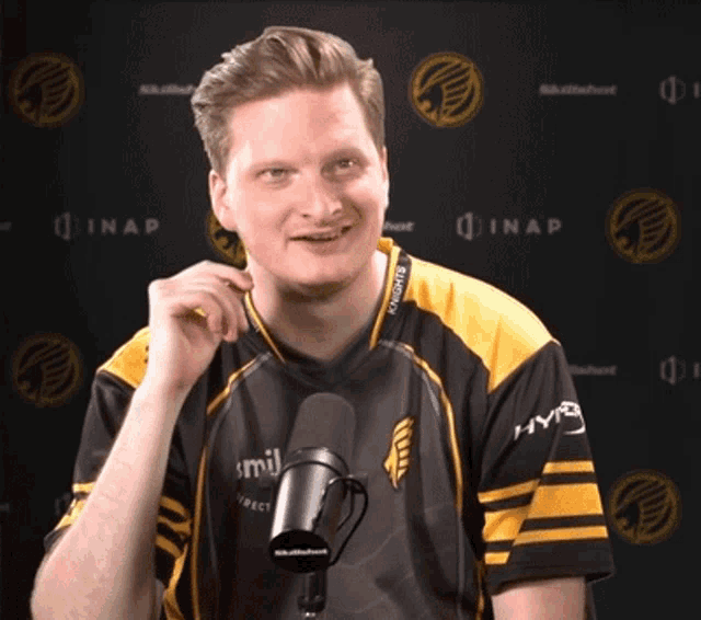 a man wearing a yellow and black shirt with hype on the sleeves stands in front of a microphone