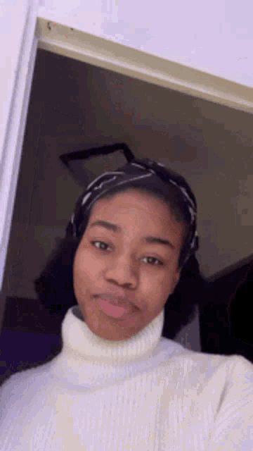 a woman wearing a white turtleneck sweater and a headband is standing in front of a door .