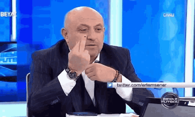 a man in a suit is giving the middle finger in front of a twitter.com/ertemsener sign