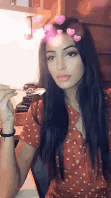 a woman with long black hair is wearing a red polka dot dress and holding a spoon .