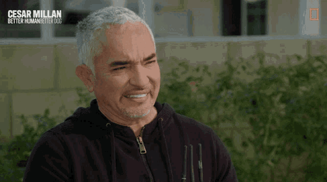 a man in a black hoodie is smiling in a national geographic video about cesar millan