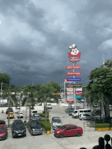 a large jollibee sign is in the middle of a parking lot surrounded by cars