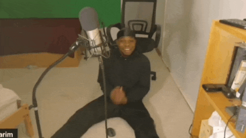 a man is sitting on the floor in front of a microphone and smiling .