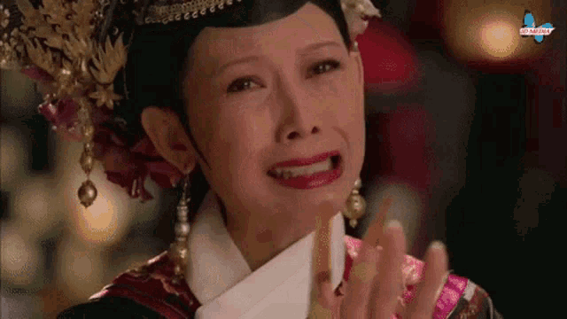 a woman with a crown on her head is crying while holding her hands up