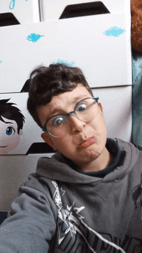a boy wearing glasses is making a funny face in front of a wall with cartoon characters on it