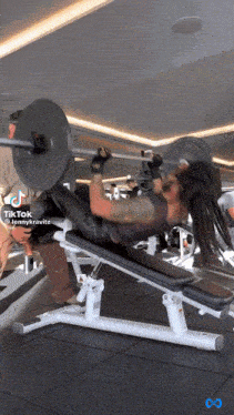 a woman is lifting a barbell in a gym with a tik tok icon above her