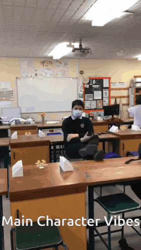 a man wearing a mask sits at a desk in a classroom with the words main character vibes written below him