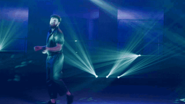 a man singing into a microphone in a dark room with green lights behind him