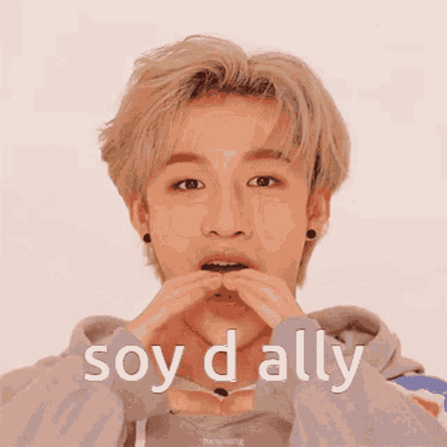 a young man is smiling and making a heart shape with his hands and the words soy d ally below him .