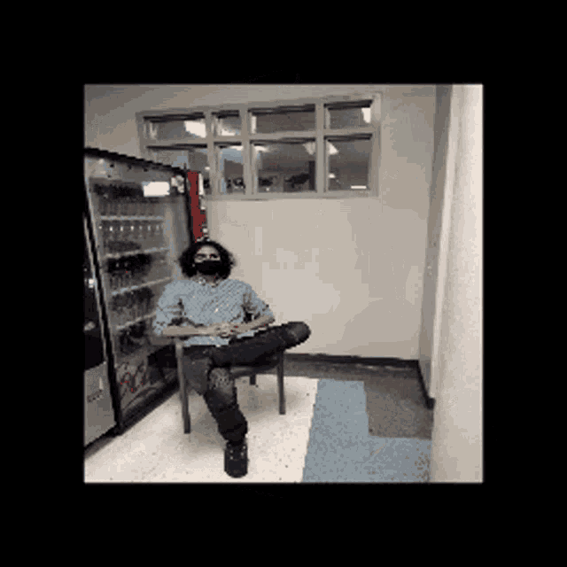 a man wearing a mask sits in a chair in front of a vending machine that says coca cola