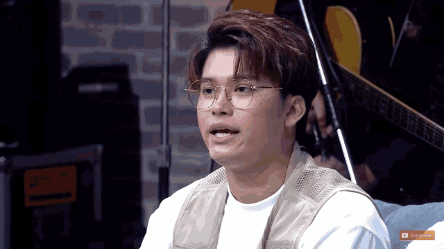 a young man wearing glasses and a vest is sitting in front of a guitar ..