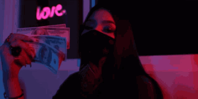 a woman wearing a mask is holding a pile of money in front of a neon sign that says love .