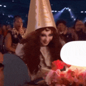 a woman wearing a cone hat with the letter d on it sits in a crowd of people