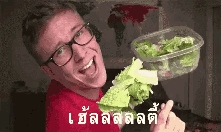a man wearing glasses is holding a plastic container of lettuce and a salad .