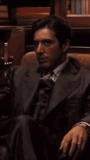 a man in a suit and tie is sitting in a chair and looking at the camera .