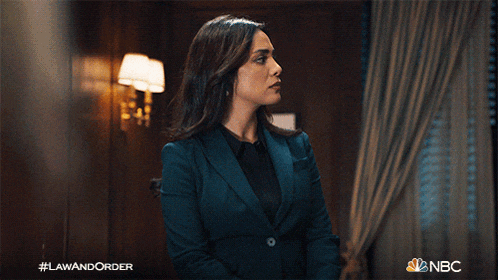 a woman in a suit stands in a room with her eyes closed and a nbc logo behind her