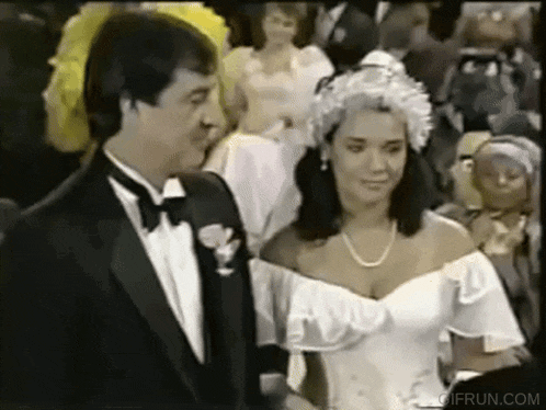 a man in a tuxedo and a woman in a wedding dress are standing next to each other in front of a crowd .