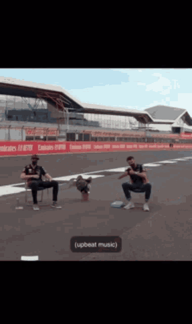 two men sit on chairs on a race track with a sign that says emirates