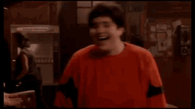 a man in a red shirt is standing in a dark room with the words `` resulto estafado '' written on the screen .