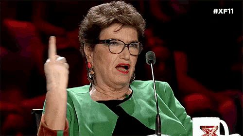 a woman wearing glasses and a green jacket is giving the middle finger in front of a microphone .