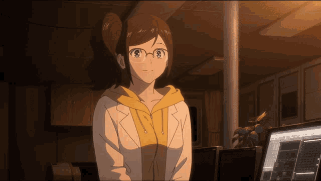 a girl wearing glasses and a yellow hoodie stands in front of a computer
