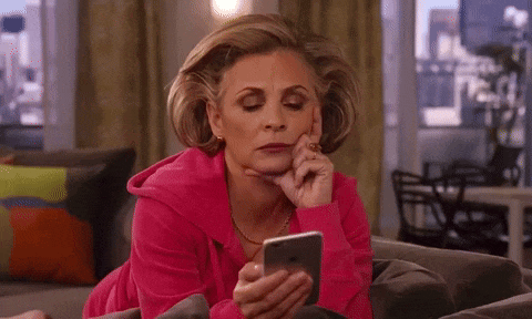 a woman in a pink sweatshirt is laying on a couch looking at her phone .