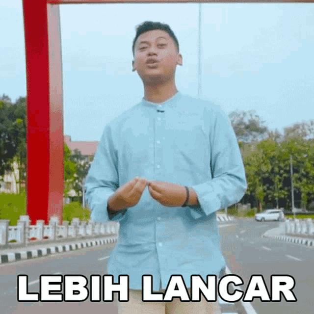 a man in a blue shirt is standing in front of a red arch and says lebih lancar