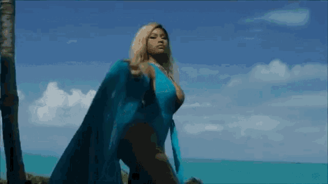 a woman in a blue swimsuit and blue cape is standing on a beach .