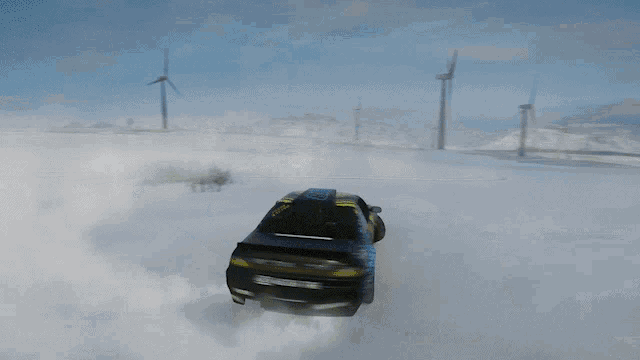 a yellow and black car is drifting in the snow with a wind turbine in the background