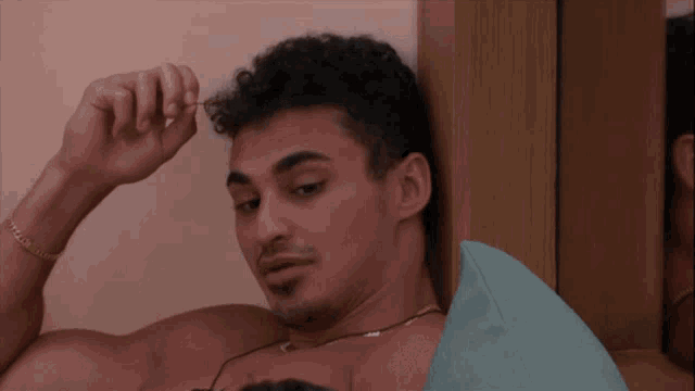 a shirtless man with a gold bracelet on his wrist looks at something