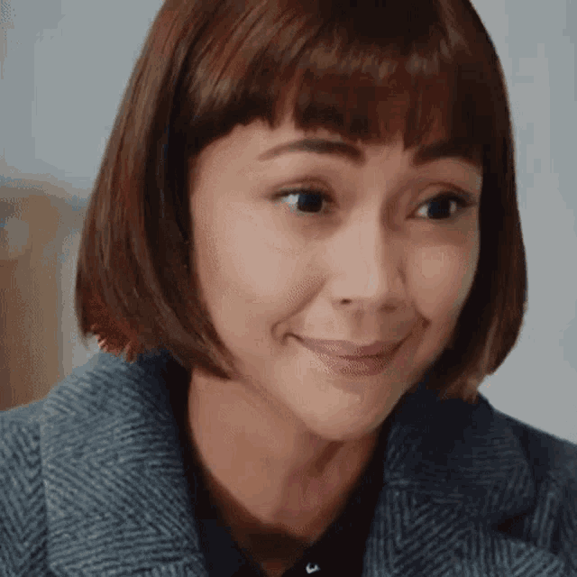 a woman with short brown hair and bangs is smiling and making a face .