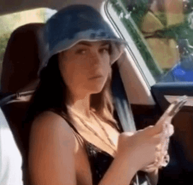 a woman is sitting in the back seat of a car wearing a bucket hat and looking at her phone .