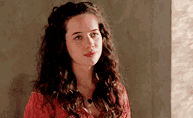 a young woman with curly hair is wearing a red shirt and necklace .