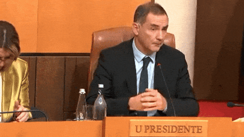 a man in a suit and tie is sitting at a table with a sign that says u presidente